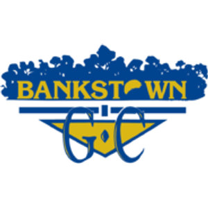 Bankstown Golf Club logo: A navy silhouette of a bushy treeline holding the word BANKSTOWN in gold capitals, whose O is drawn as a golf ball with a navy crescent shadow, above a navy horizontal bar and a wide gold downward-pointing triangle outlined in navy with a small gold diamond at its centre, overlaid by a large navy script G and C.