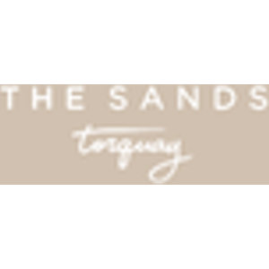 Torquay Sands Golf Club logo: THE SANDS in widely letterspaced white capitals above torquay in a white handwritten script with a looping flourish, on a solid sand-beige square.