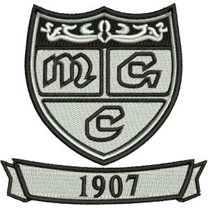 Muskogee Golf Club logo: A gray and black embroidered-style shield crest divided into panels with the Old English letters 'M', 'G' and 'C', an ornamental scroll across the top and a ribbon banner reading '1907' below.