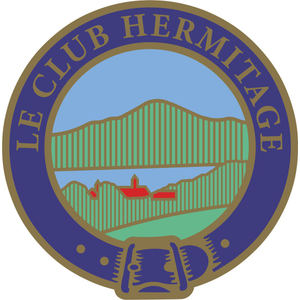 Hermitage Golf Club logo: A circular Scottish clan-style badge with a gold rope-edged outer ring and a navy band lettered LE CLUB HERMITAGE in gold, enclosing a green ridged mountain above a blue lake with small red-roofed buildings, and a gold-buckled navy belt strap across the foot of the badge.
